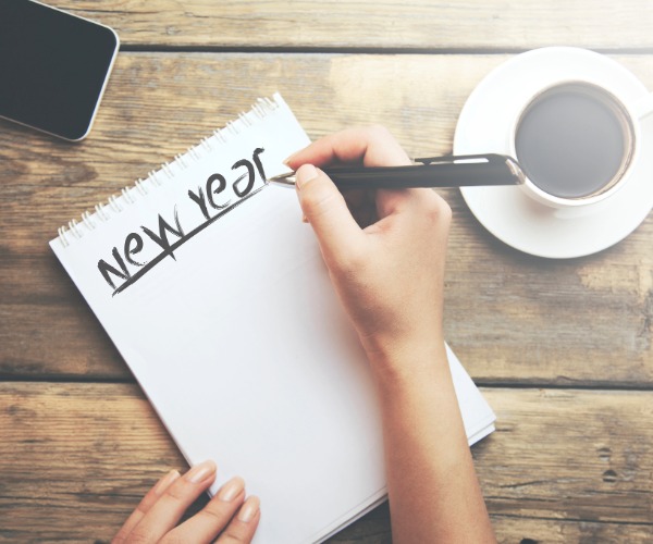 Female hand writing "New Year" with a black pen on a note pad.
